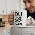 Weisse Tasse mit dem schwarzen Aufdruck Du bist nicht allein 